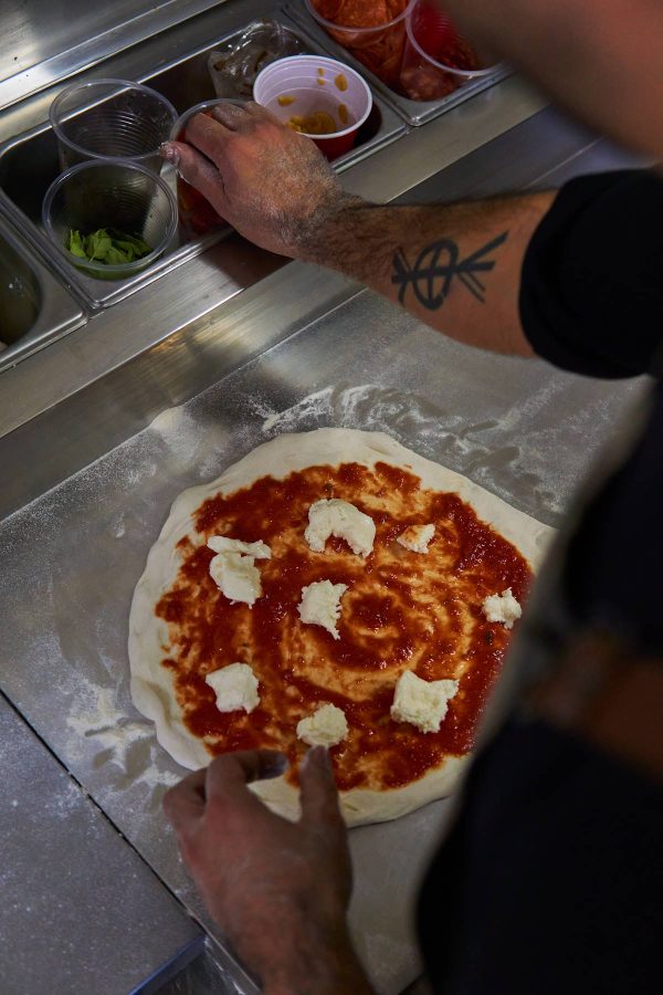 Manos de pizzero añadiendo queso fior di latte a una pizza napoletana.